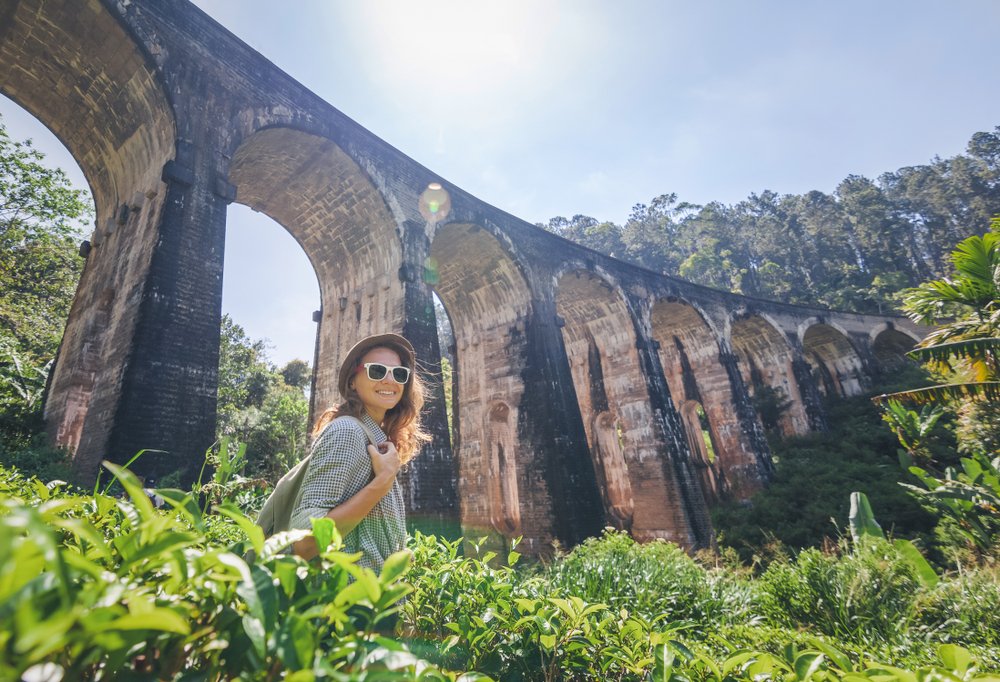 Traveller pausing for a photo beneath the Nine Arches Bridge in Ella